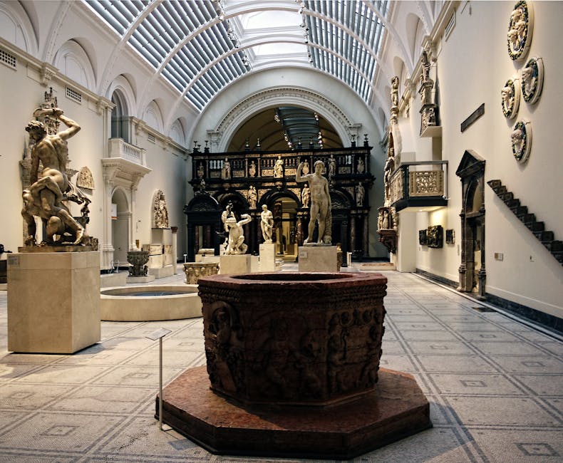 A spacious interior view of the Victoria and Albert Museum featuring a high, curved glass ceiling with bright natural light streaming through. The ceiling is supported by white, evenly spaced steel ribs, creating a symmetrical pattern above. The image captures the long corridor with white walls and decorative sculptures placed along the sides. The polished, reflective floor creates a mirror-like effect, showing an inverted reflection of the ceiling structure and the corridor below. The environment appears clean and well-lit, emphasizing the architectural detail of the museum's interior, which is relevant to house removals and moving services focused on precise packing and careful transport of valuable artworks or furniture within cultural institutions or private homes heading for collections or exhibitions. Brompton Man and Van occasionally associates such interior spaces with professional removal and furniture transport processes involved in home relocation or institutional moves.